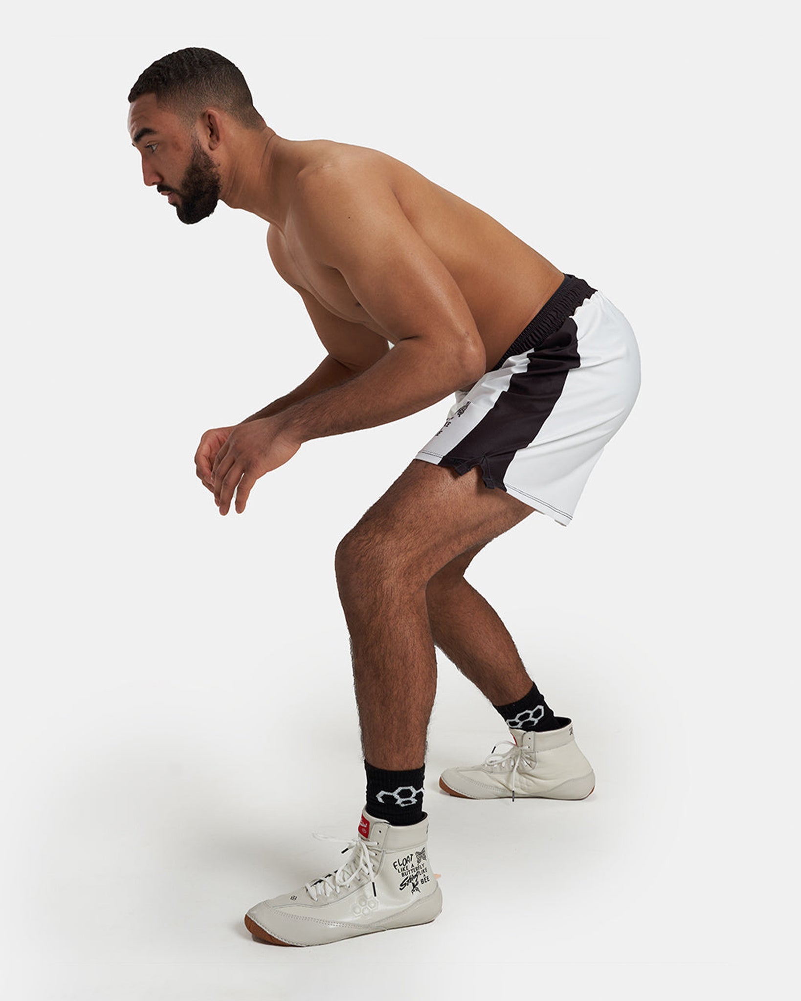 A muscular man prepares to jump while wearing black and white athletic shorts and sneakers with socks showcasing an intense athletic pose