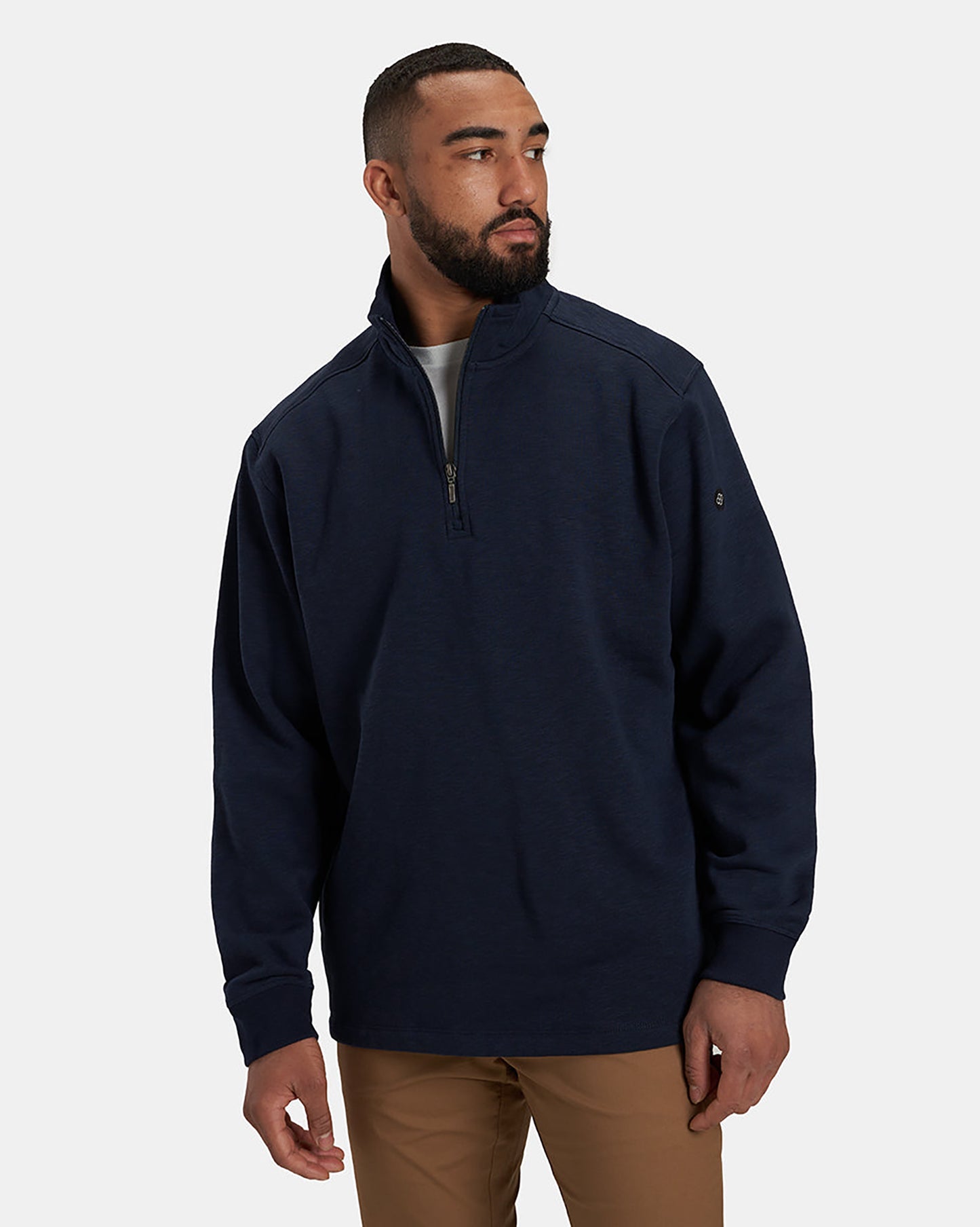 A man wearing a navy blue half-zip pullover sweater paired with tan pants stands against a neutral background showcasing a casual and comfortable style