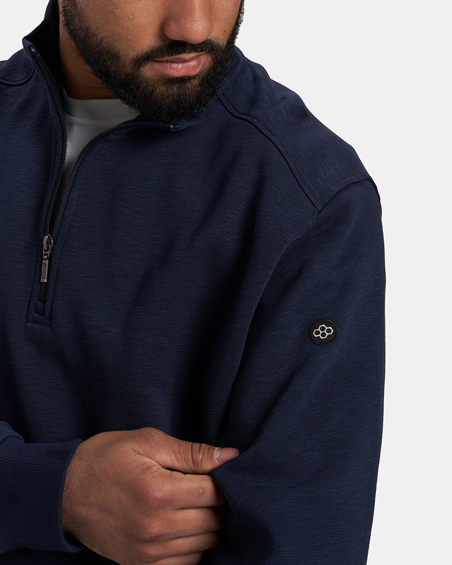 A close-up of a man wearing a navy blue zippered pullover showcasing a subtle texture and a logo on the sleeve