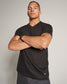 A confident model posing with crossed arms wearing a fitted black V-neck shirt showcasing a muscular physique against a neutral background