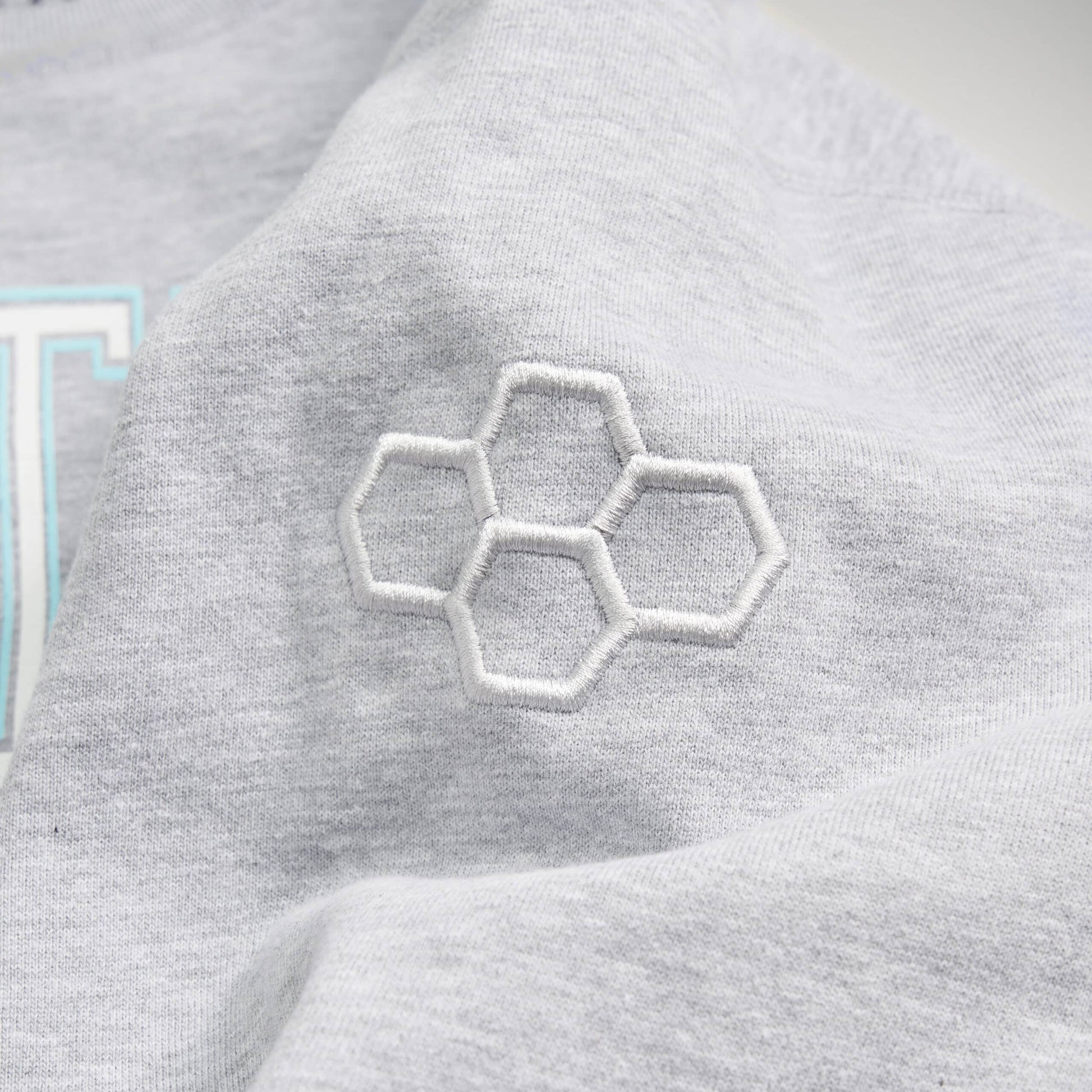 A close-up view of a light gray garment featuring an intricate white embroidered hexagon design on the sleeve