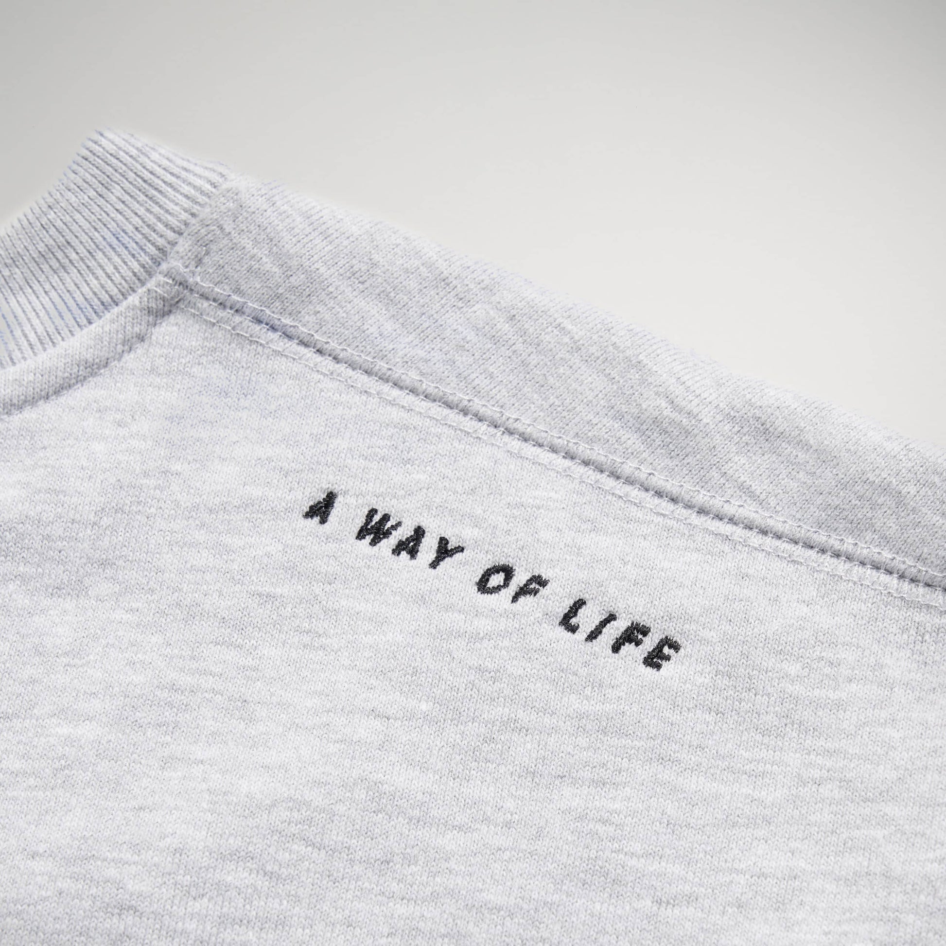 Close-up view of the collar area of a light gray sweatshirt featuring the phrase A WAY OF LIFE embroidered in black