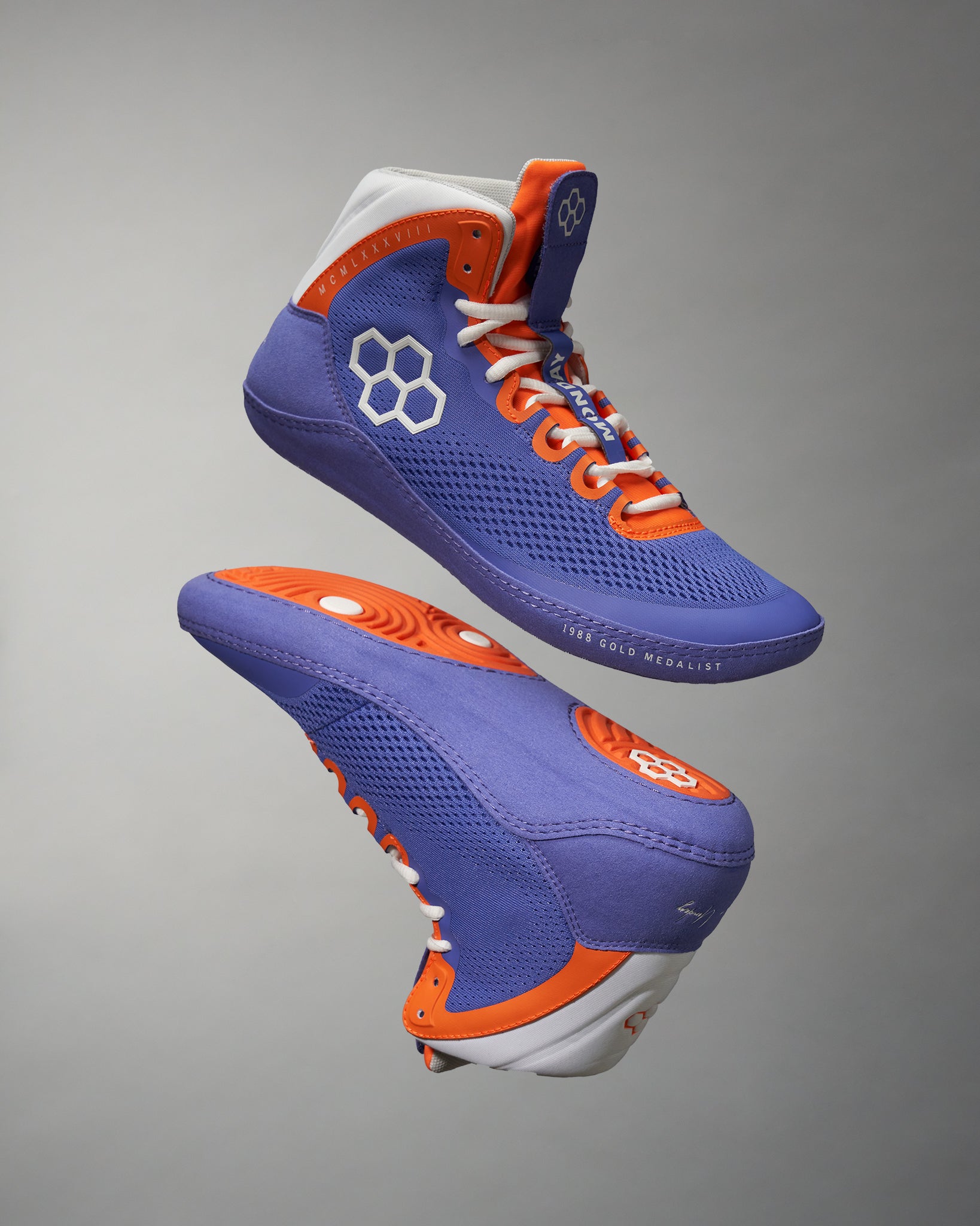 A pair of vibrant purple high-top athletic shoes with orange accents featuring a hexagonal logo and showcasing a modern design for performance and style