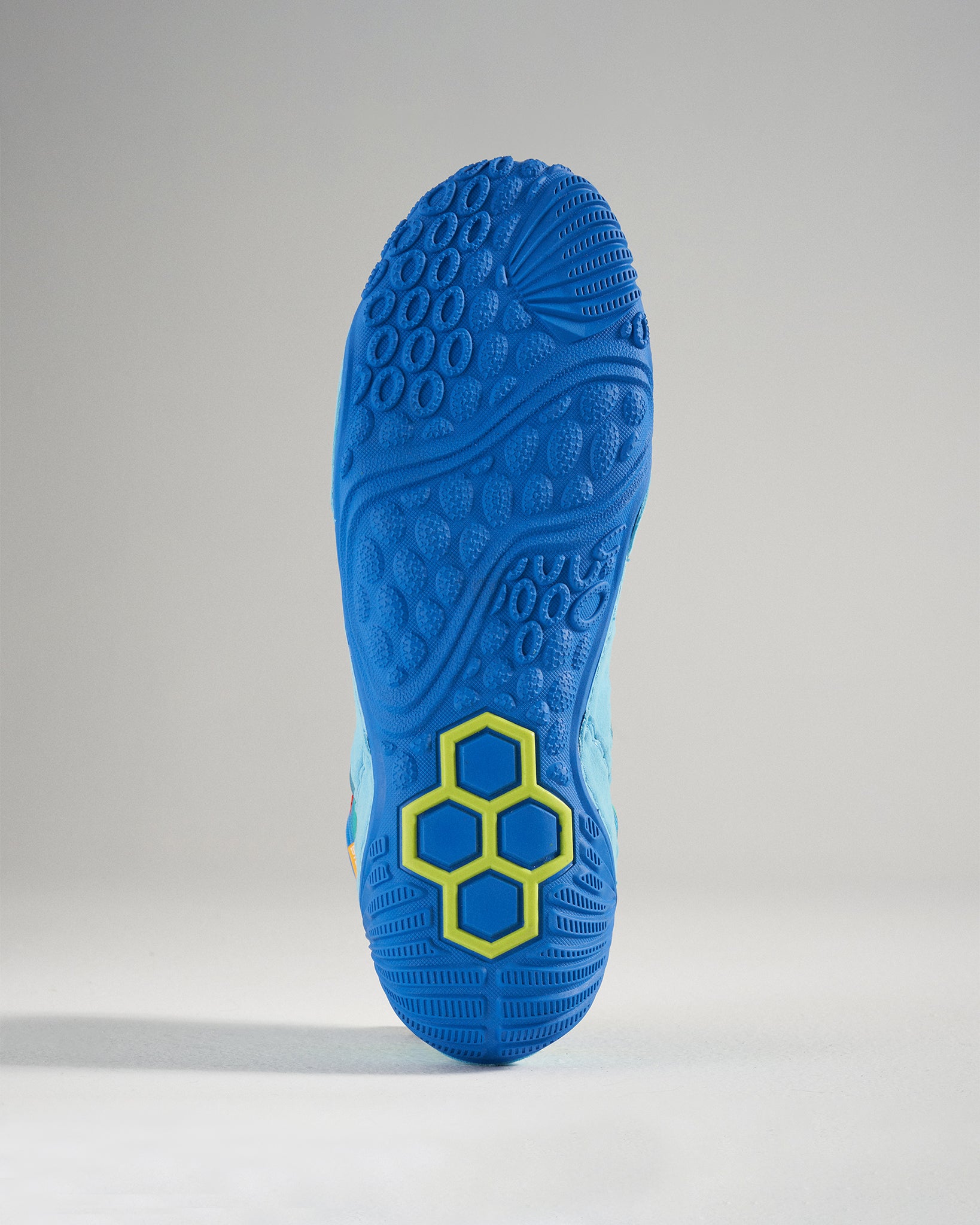 The image presents a close-up view of a brightly colored athletic shoe sole featuring a textured blue surface with distinctive grip patterns and a yellow hexagonal design element