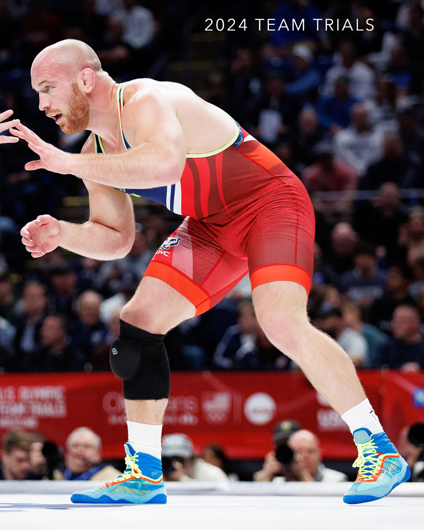 A wrestler in a red singlet competes at the 2024 Team Trials showcasing dynamic motion and a focus on his opponent