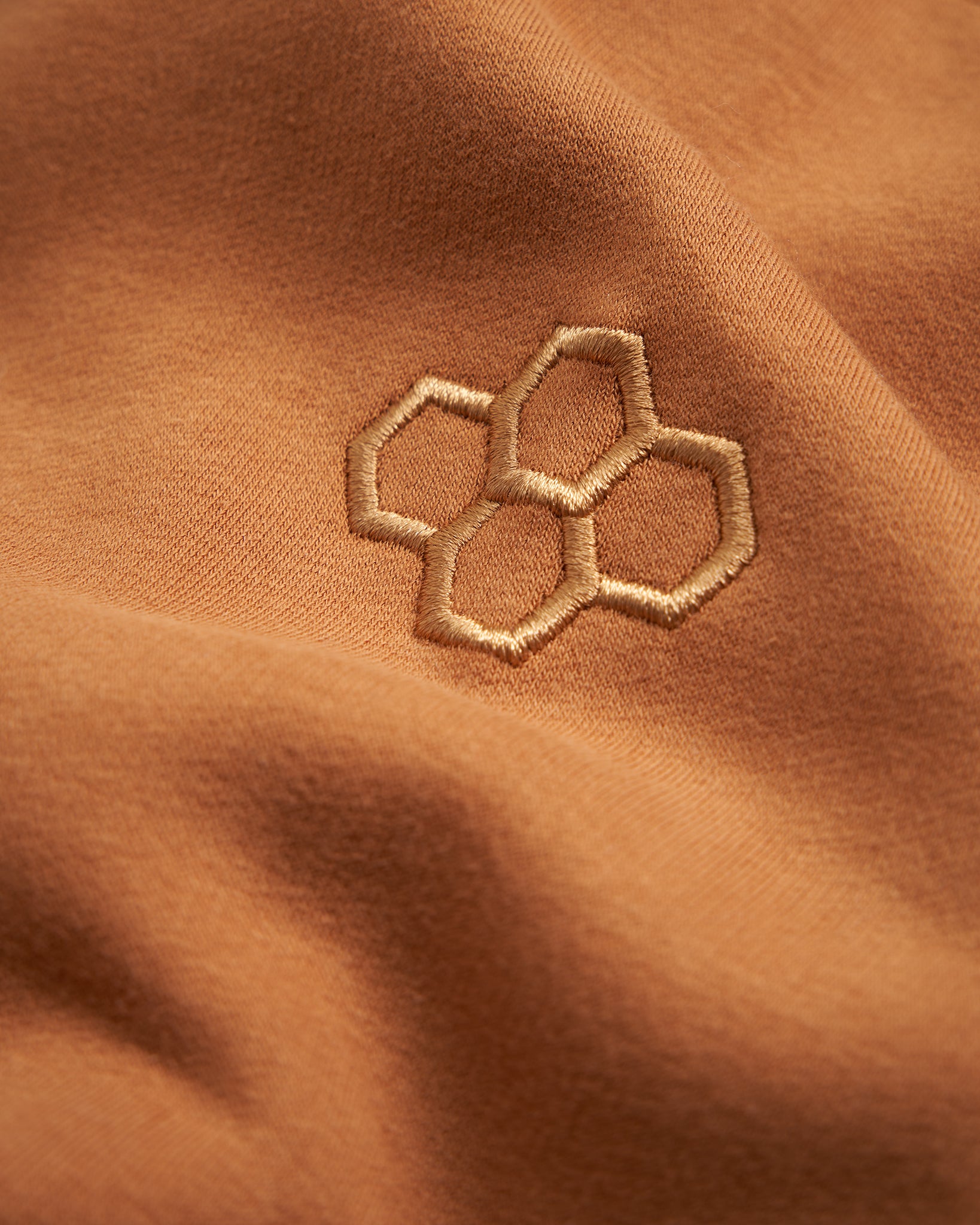 Close-up of a soft warm-toned fabric featuring an embroidered honeycomb design in a complementary color