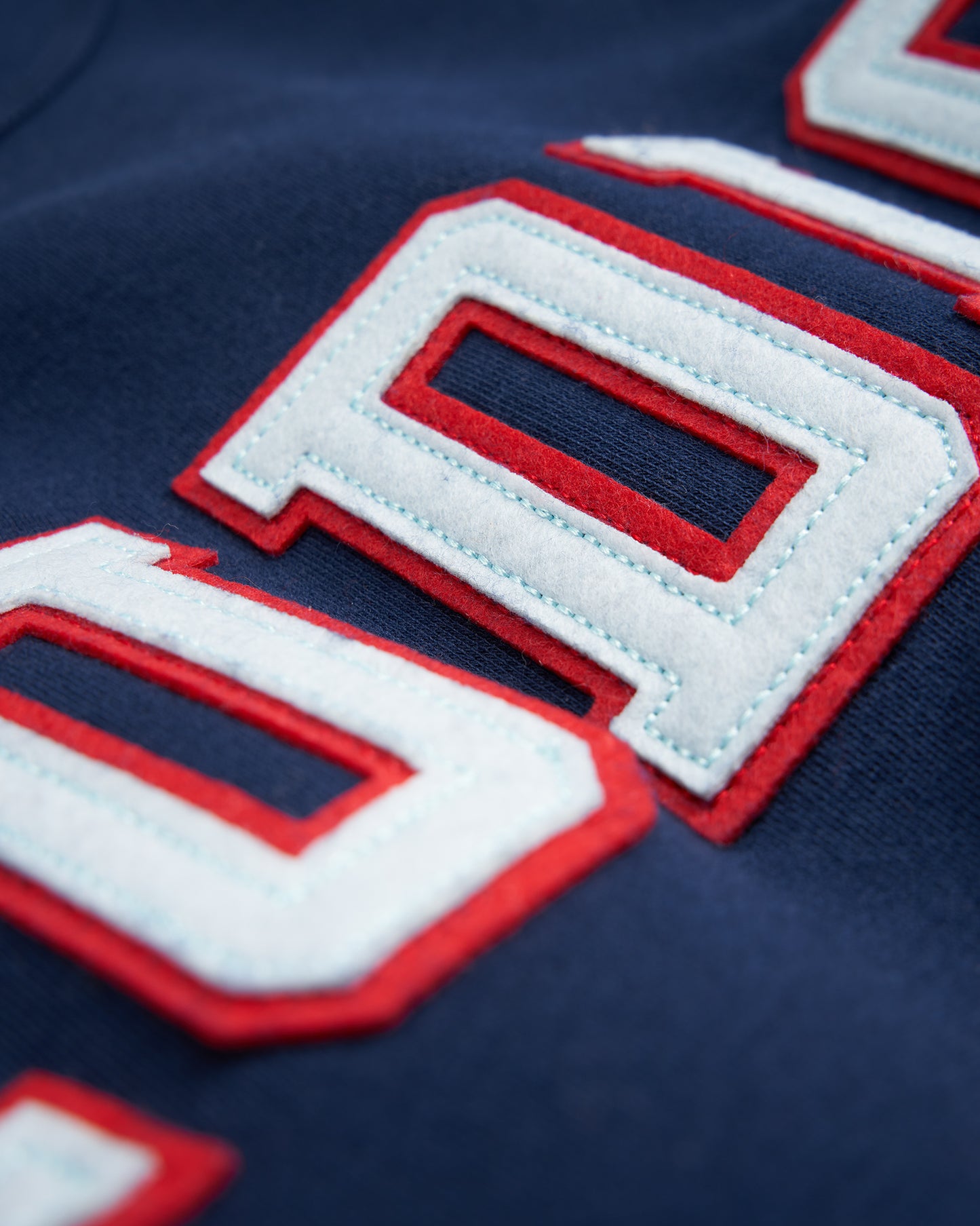 A close-up view of a navy blue sweatshirt featuring bold stitched letters in red and white showcasing a three-dimensional texture that emphasizes the craftsmanship of the garment