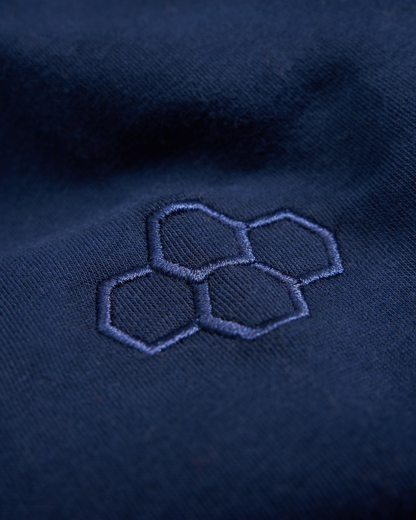 A close-up of a dark blue fabric featuring a subtle navy embroidered hexagonal pattern highlighting its texture and design details