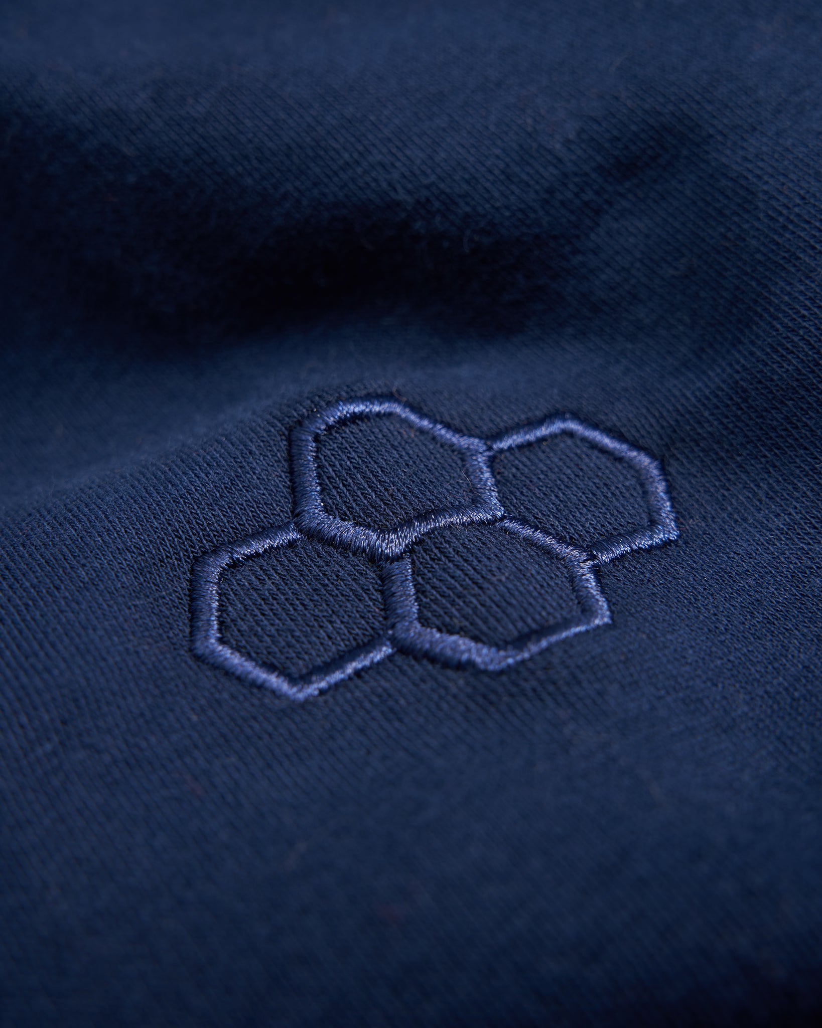 A close-up of a dark blue fabric featuring a subtle navy embroidered hexagonal pattern highlighting its texture and design details