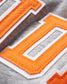 Close-up of a gray fabric featuring bold orange and white felt appliqué lettering with intricate stitching