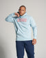 A man poses confidently in a light blue hoodie with RUDIS printed across the chest paired with navy sweatpants in a neutral background