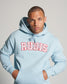 A male model in a light blue hoodie with RUDIS printed in bold red letters striking a serious expression with his hands in his pockets