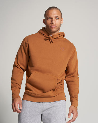 A man stands confidently wearing a rust-colored hoodie paired with gray sweatpants presenting a casual yet stylish look