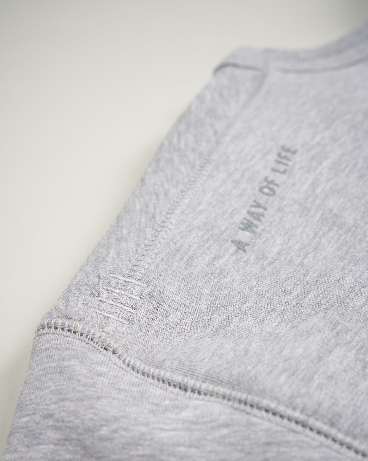 A close-up view of a gray sweatshirt sleeve featuring the phrase A WAY OF LIFE printed on it highlighting its soft texture and seam details