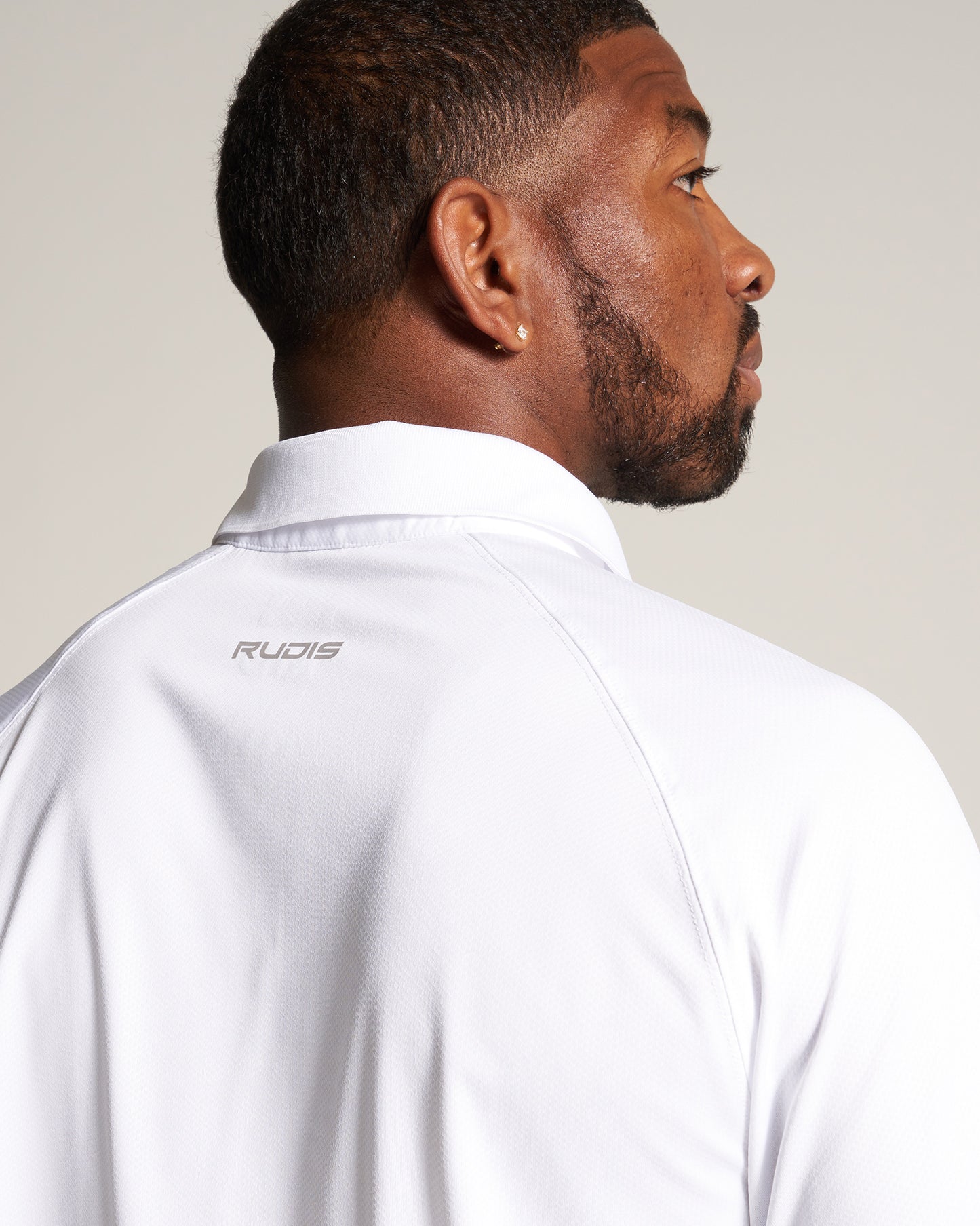 A close-up view of a man in a white athletic shirt showcasing the brand logo RUDIS on the back of the collar and his profile from the side