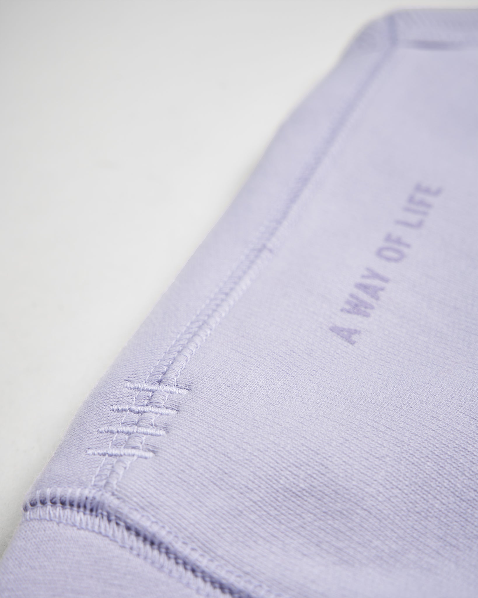 A close-up of a lavender-colored fabric showcasing its texture and stitched detail with the text A WAY OF LIFE