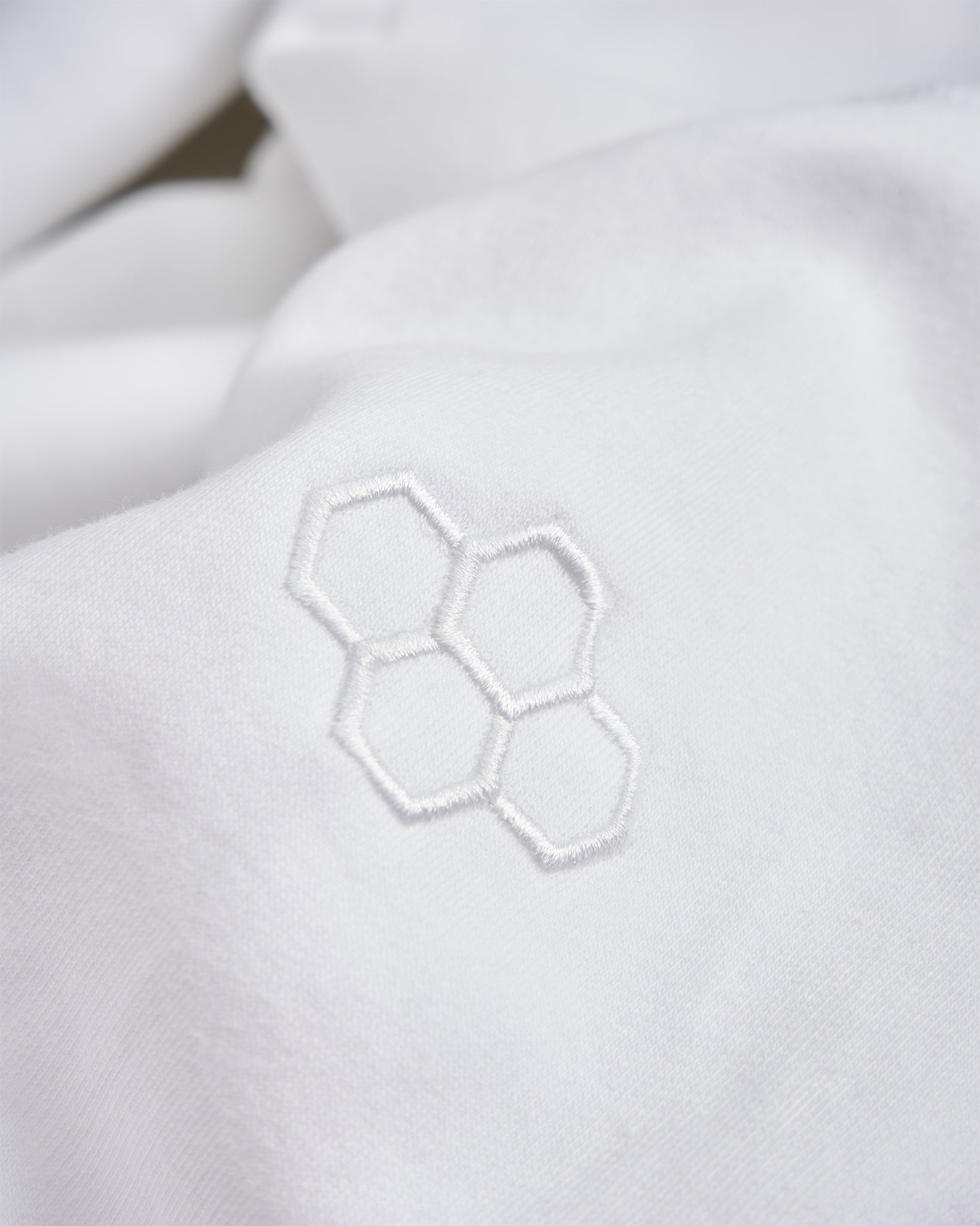 A close-up view of a white fabric featuring a subtle embroidered hexagonal pattern highlighting its soft texture and minimalist design