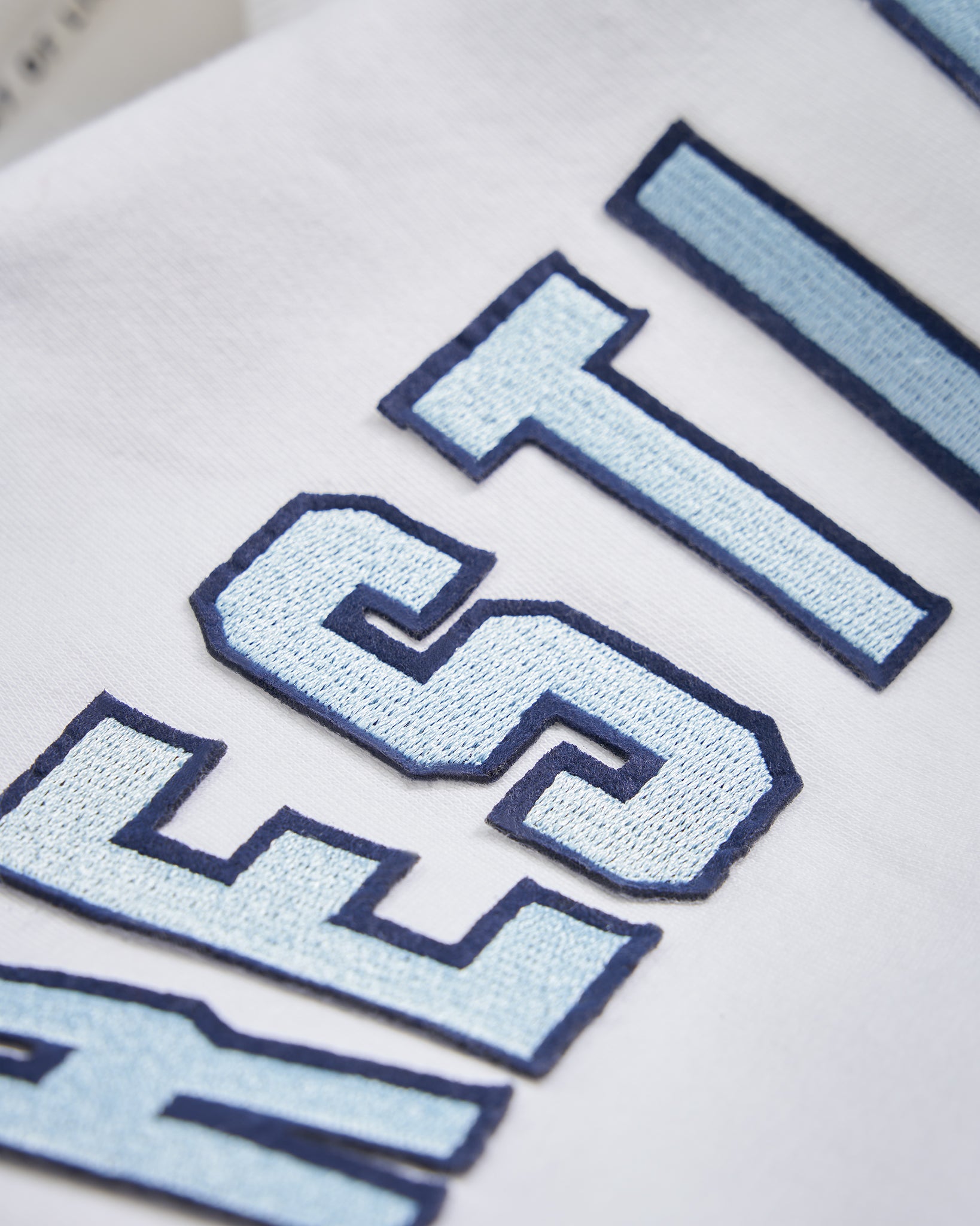 This image features a close-up of stylized embroidered text on a white fabric highlighting layered blue tones and a textured finish