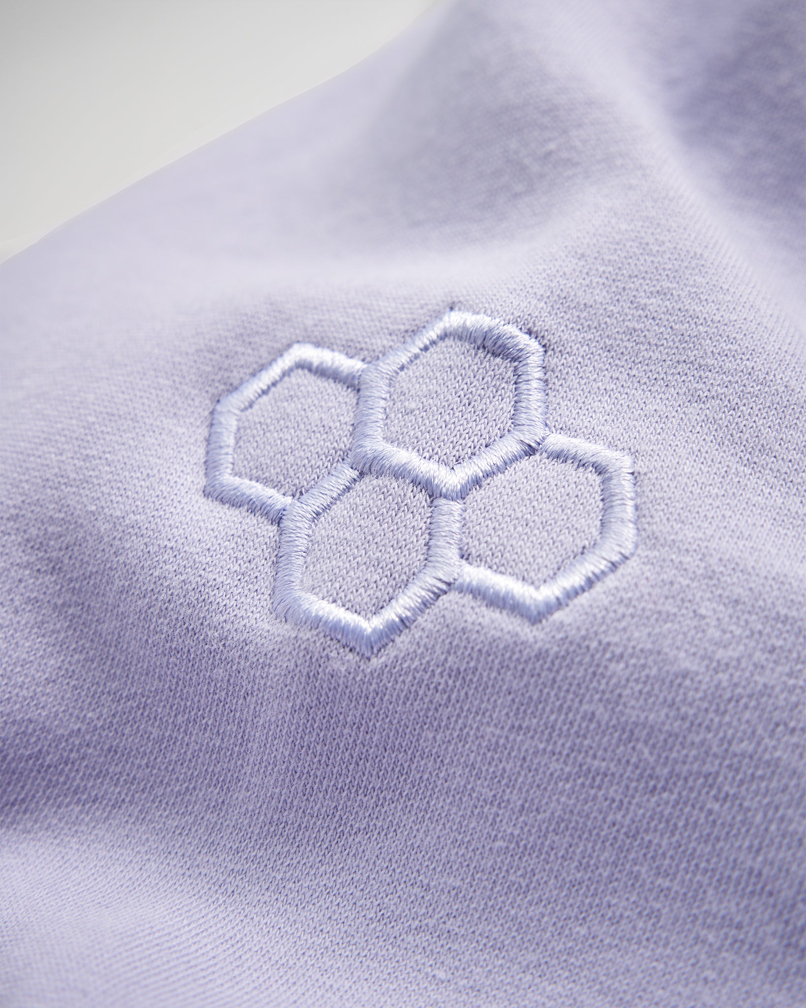 A close-up view of a soft lavender fabric featuring a stylized embroidered honeycomb design in light blue thread