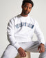 A man poses in a white sweatshirt with WRESTLING printed prominently on the front sitting casually on a wooden block while wearing gray sweatpants