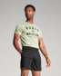 A confident man wearing a light green T-shirt with RUDIS WRESTLER printed on it and black athletic shorts posing against a neutral background