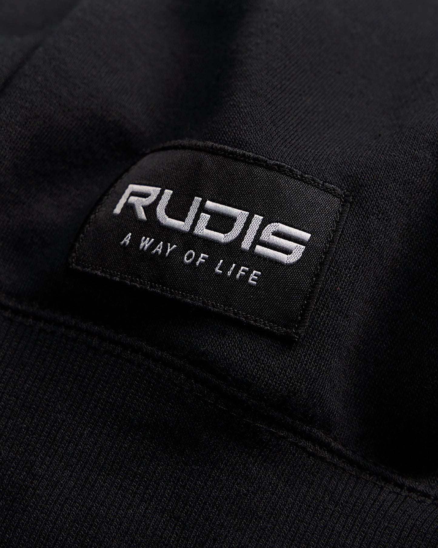 A close-up view of a black fabric patch featuring the brand name RUDIS and the tagline A WAY OF LIFE in white lettering