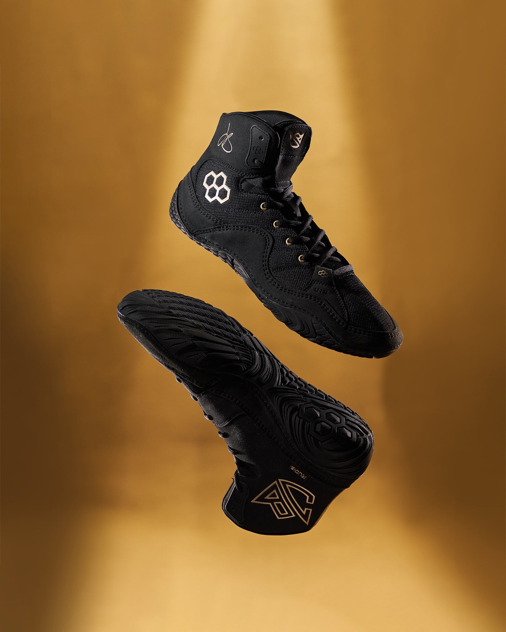 This image features a dynamic pair of black high-top athletic shoes displaying intricate design elements and a gold accent against a golden backdrop