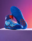 Vibrant blue athletic shoes with intricate designs and a textured sole showcased on a light pedestal against a gradient background