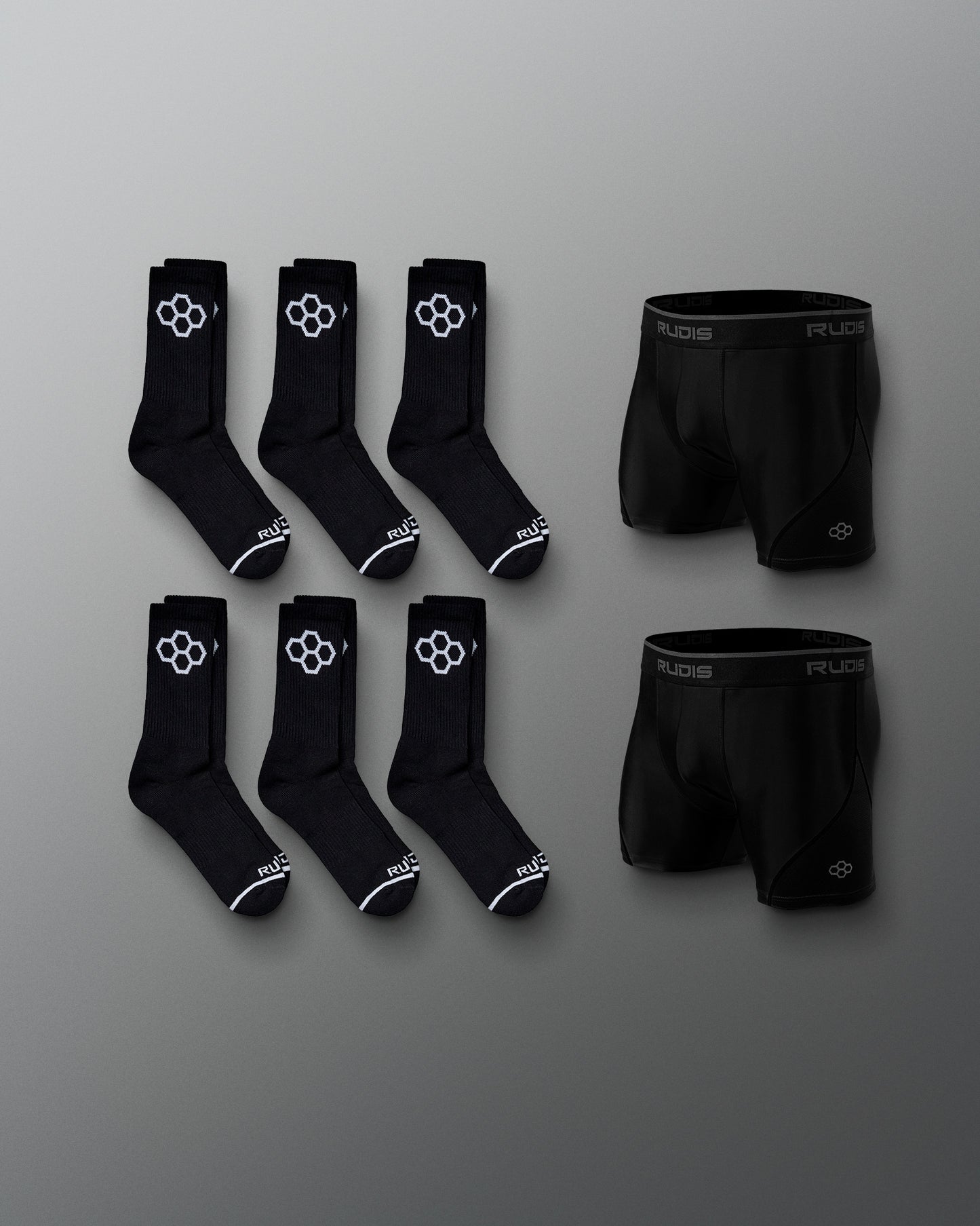 Six pairs of black athletic socks and a pair of black boxer briefs, both showcasing a white logo, are presented against a soft gray background.