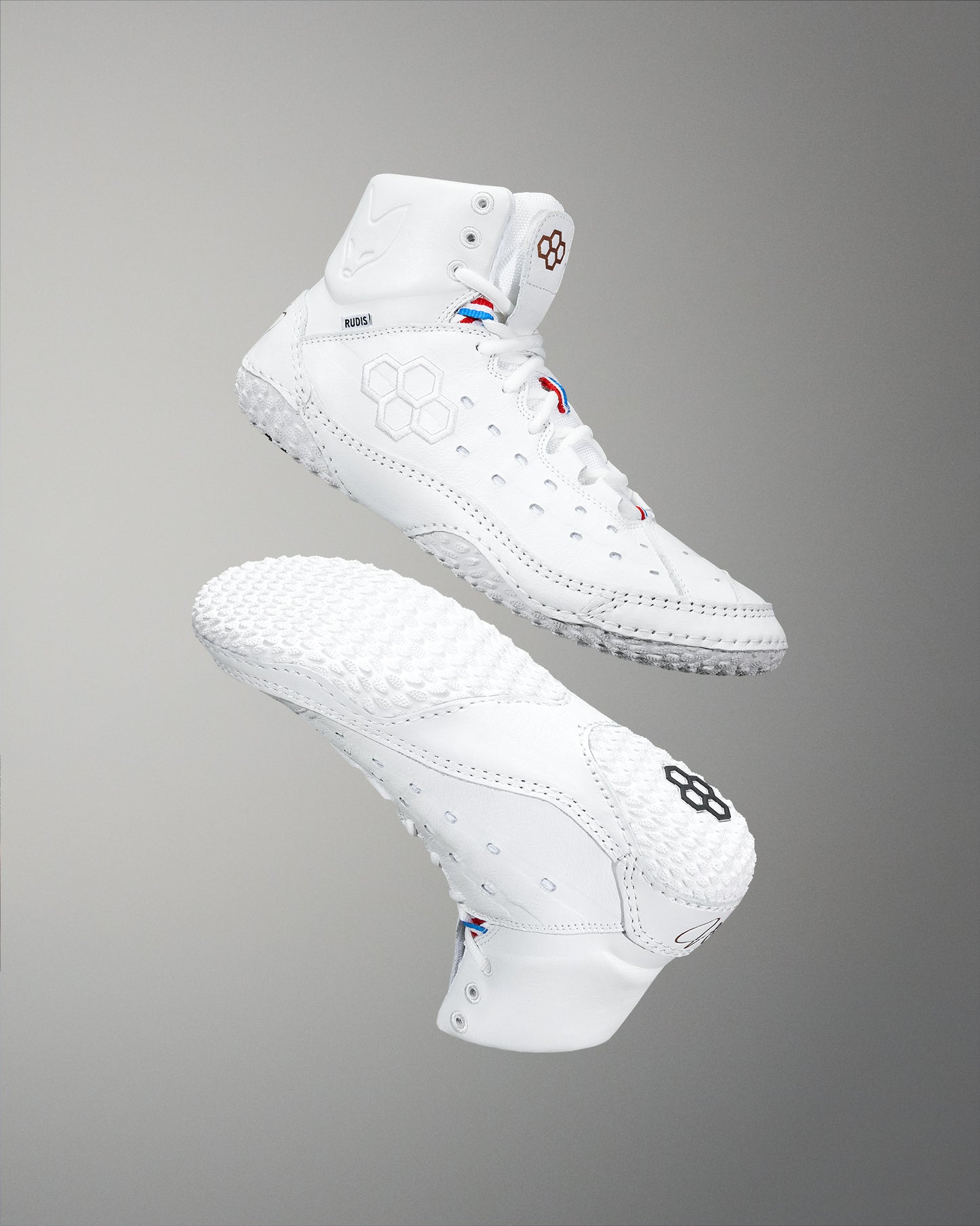 White high-top athletic shoes with textured soles and hexagonal designs are shown floating against a gray background, highlighting their smooth design and performance features.