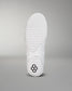 The sole of a white shoe, featuring a textured grip surface and a small black hexagonal logo, is set against a soft gray background.