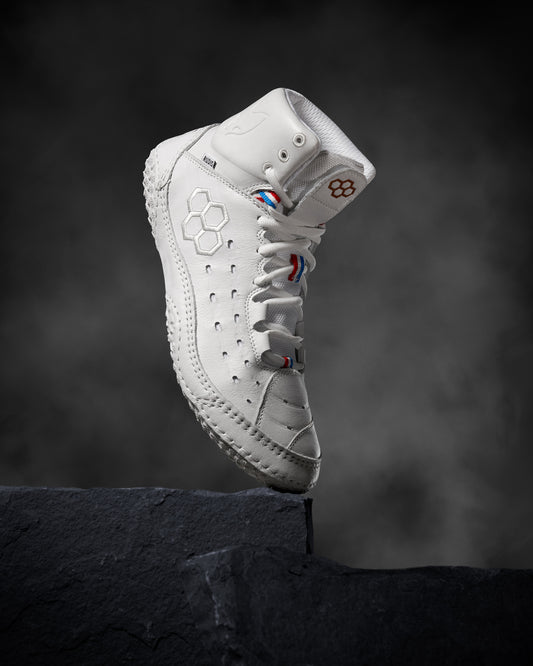 A high-top white athletic shoe with detailed stitching and colorful accents is perched on a black rock, highlighted by a smoky background.