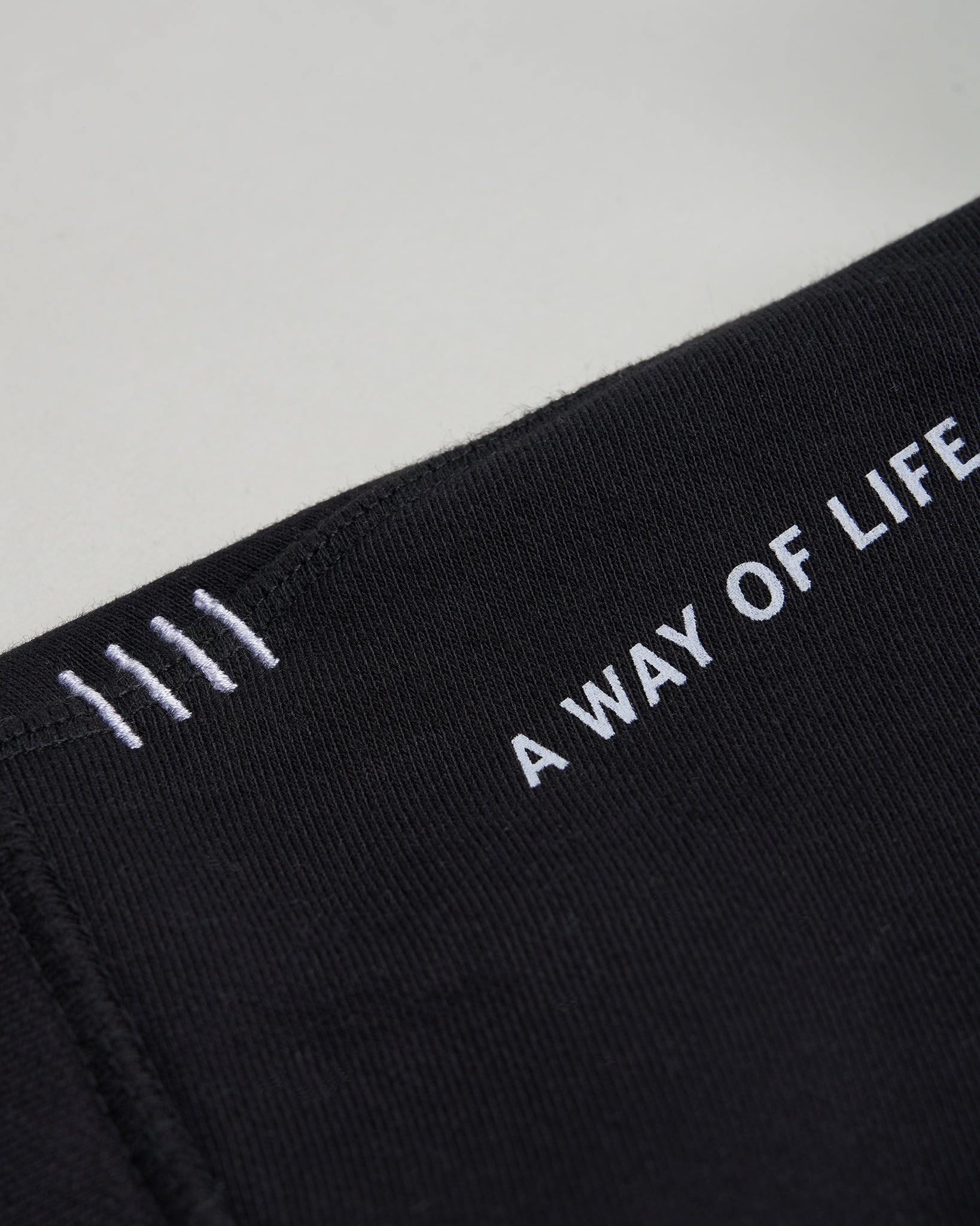 Close-up view of a black fabric featuring white embroidered text that reads A WAY OF LIFE with three vertical lines above it