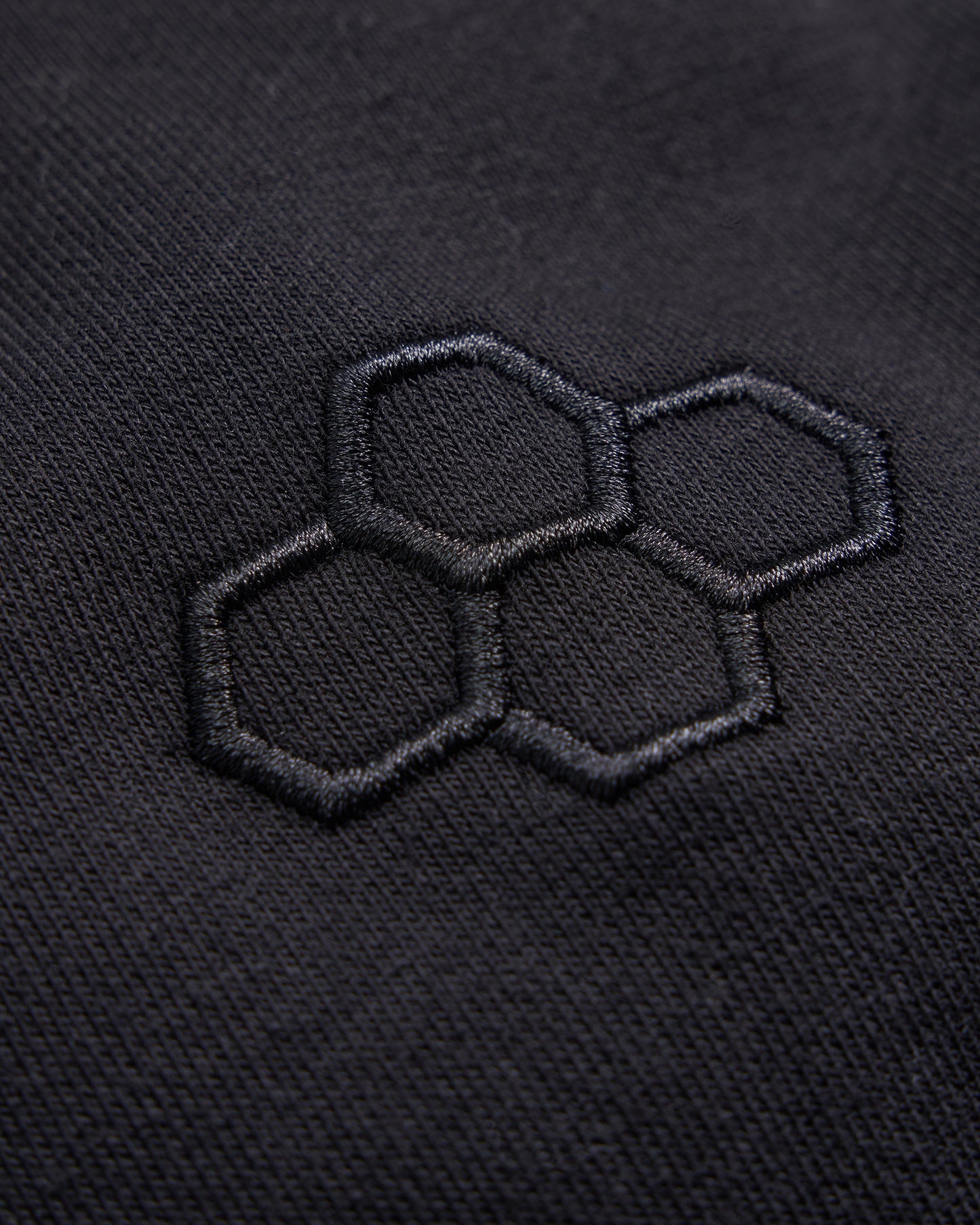 An intricate embroidered logo featuring three hexagons on a textured black fabric background highlighting a modern and minimalistic design approach