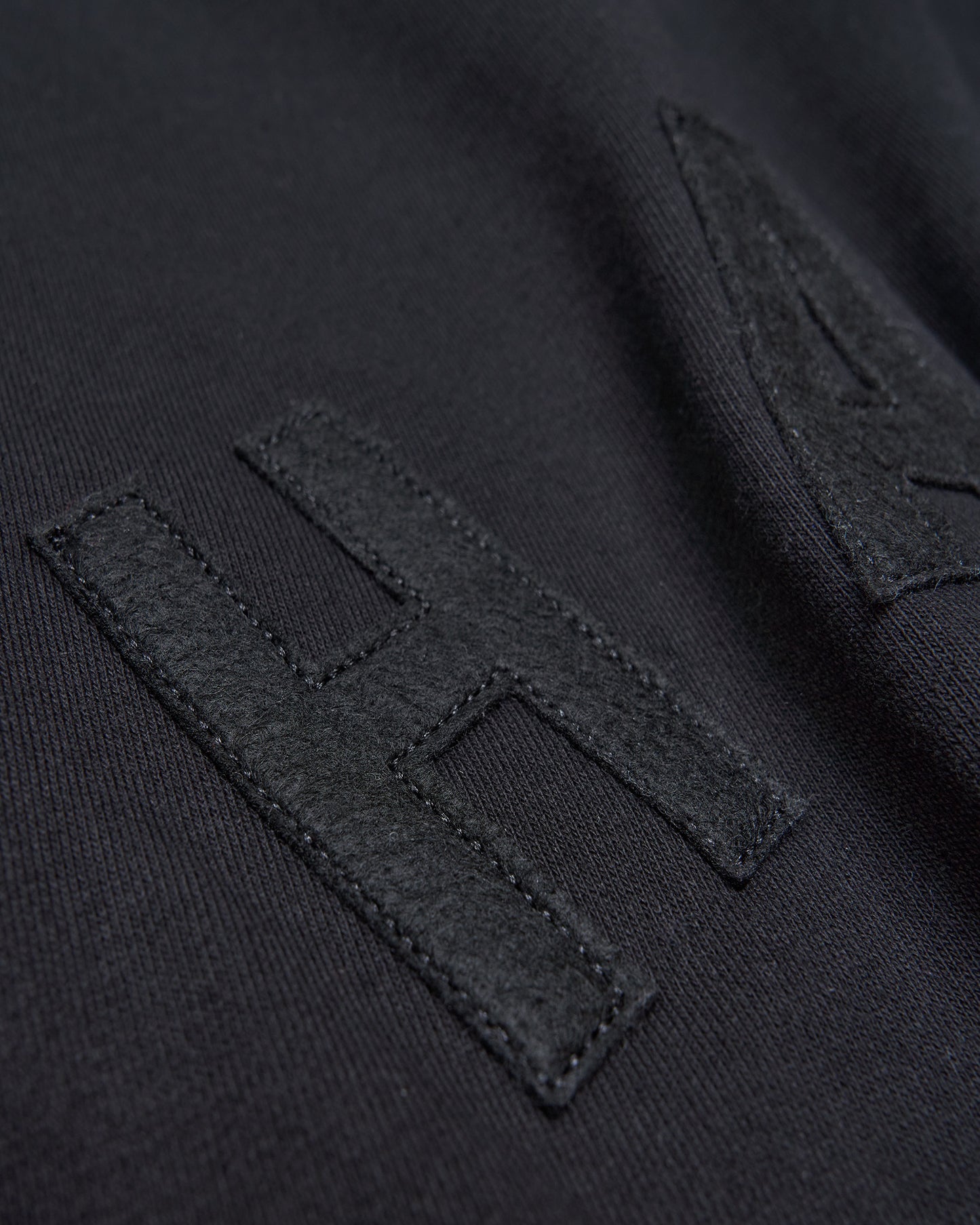 Close-up of a black fabric surface featuring a prominent textured letter H stitched in a contrasting fabric