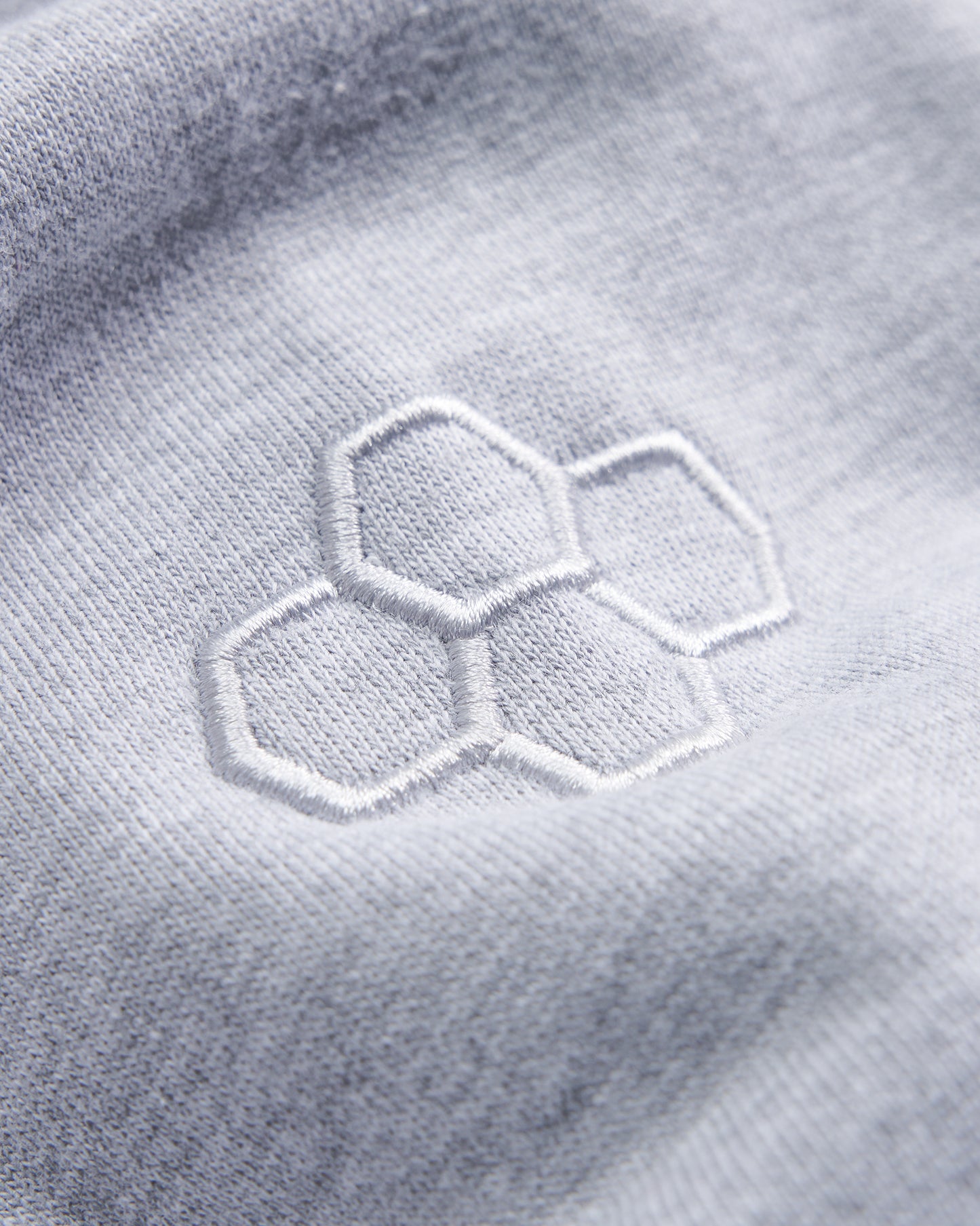 A close-up view of a light gray fabric featuring an embroidered hexagonal logo in white showcasing the textiles texture and quality