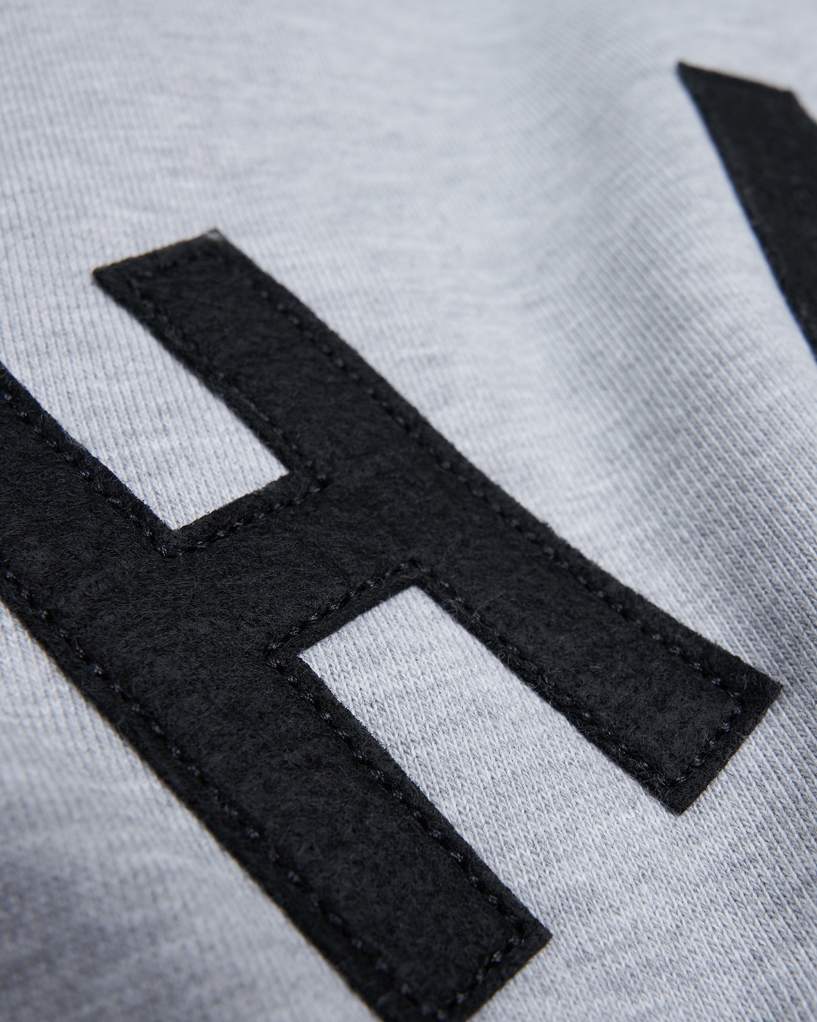 A close-up view of a gray fabric featuring a large black felt lettering emphasizing texture and detail