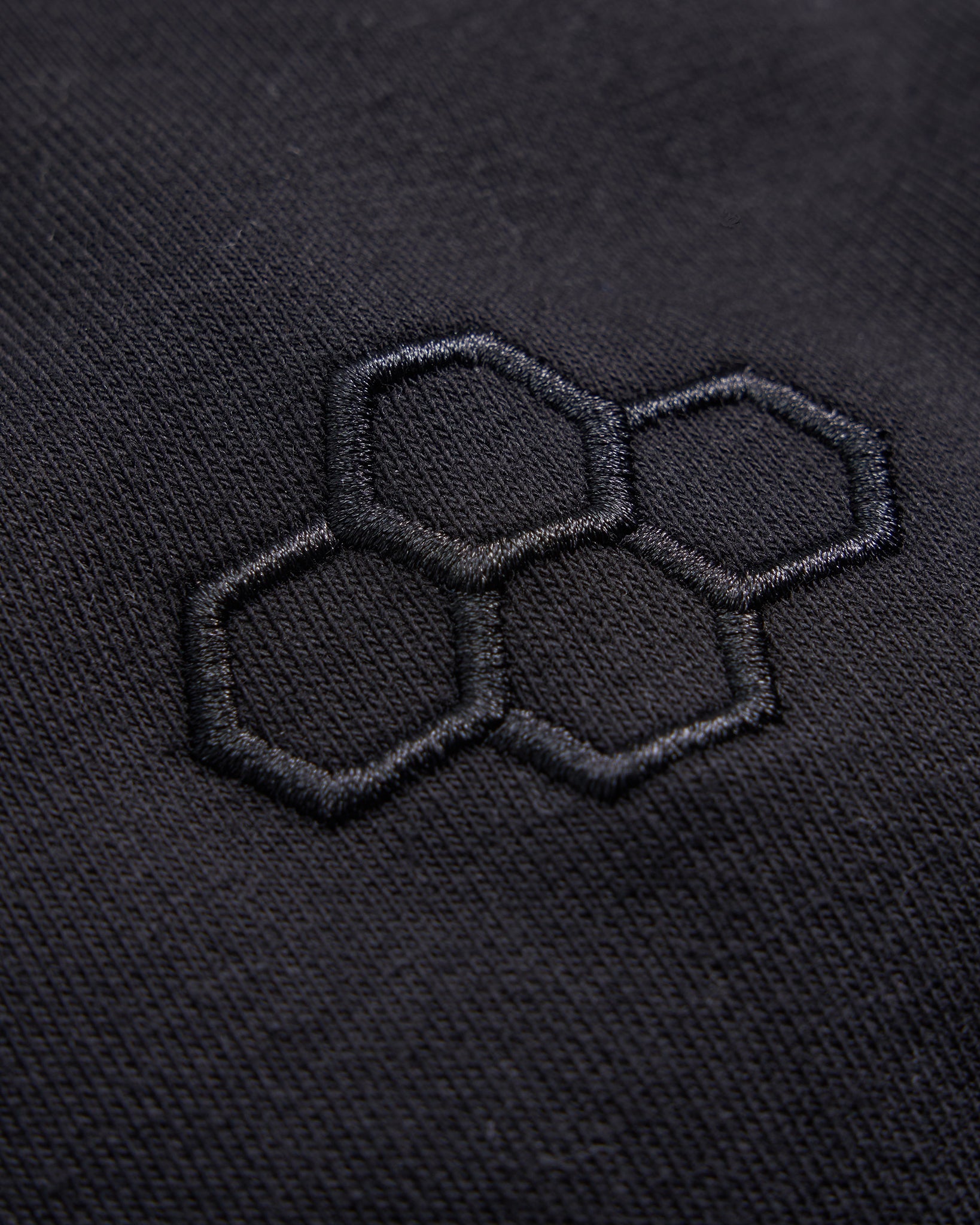 This image features a close-up of a textured black fabric with an embroidered hexagonal design highlighting the intricate stitching