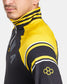 A close-up view of a man wearing a black and yellow athletic jacket with distinctive striped details and a logo on the sleeve