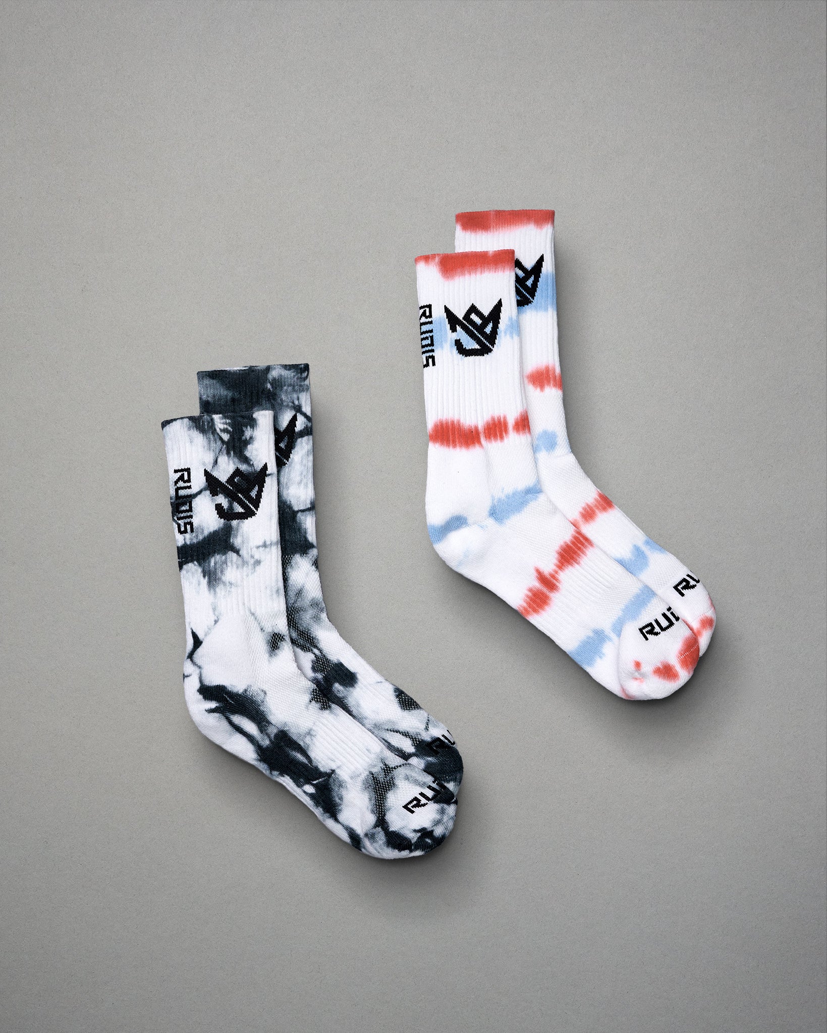 A pair of colorful tie-dye socks featuring black and white patterns alongside a red white and blue design both with a distinctive logo