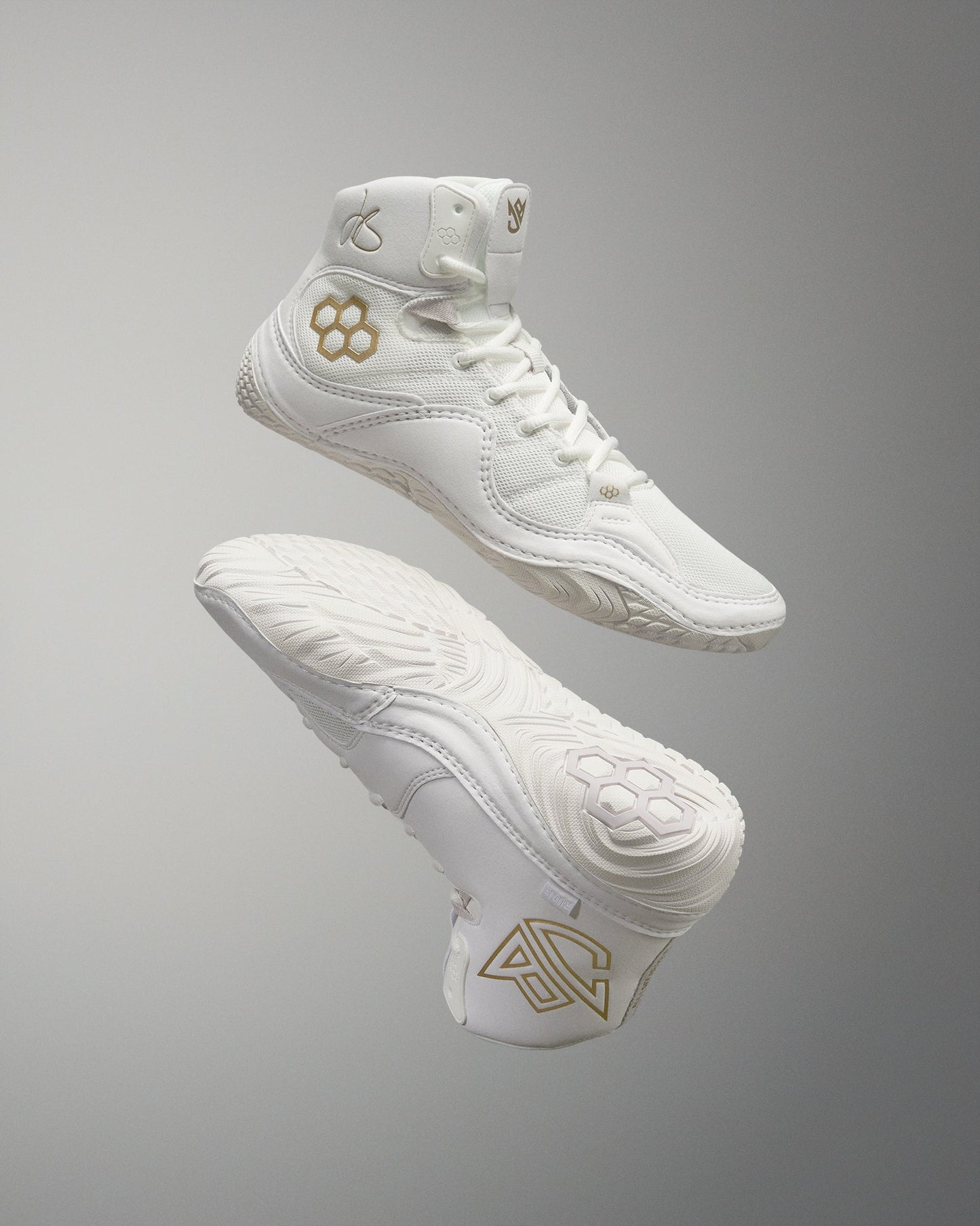 White high-top sneakers with textured design and gold accents are seen floating against a soft gray background, showcasing their athletic features.