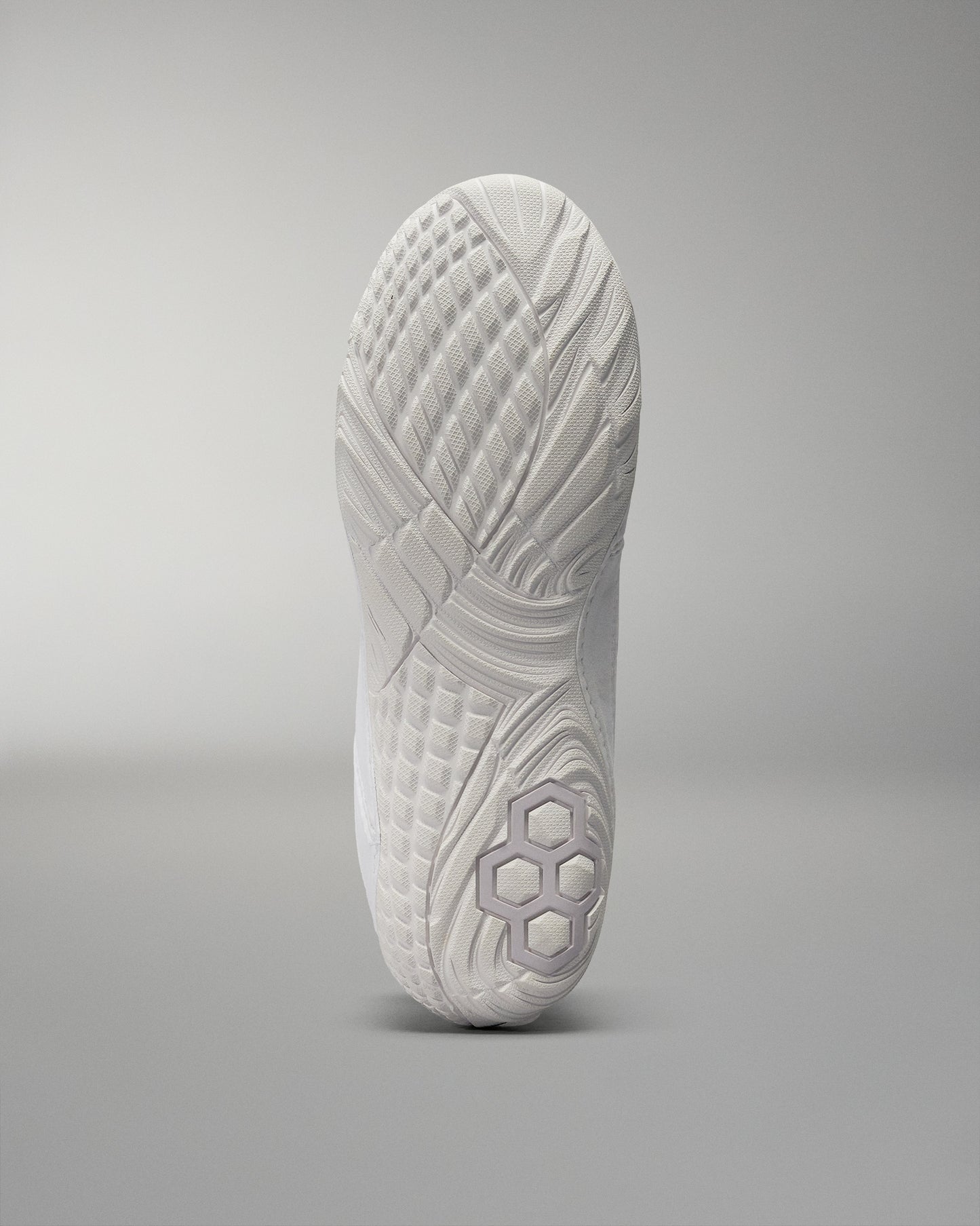 The shoe's sole presents a textured white design with geometric patterns for improved grip against a soft gradient background.