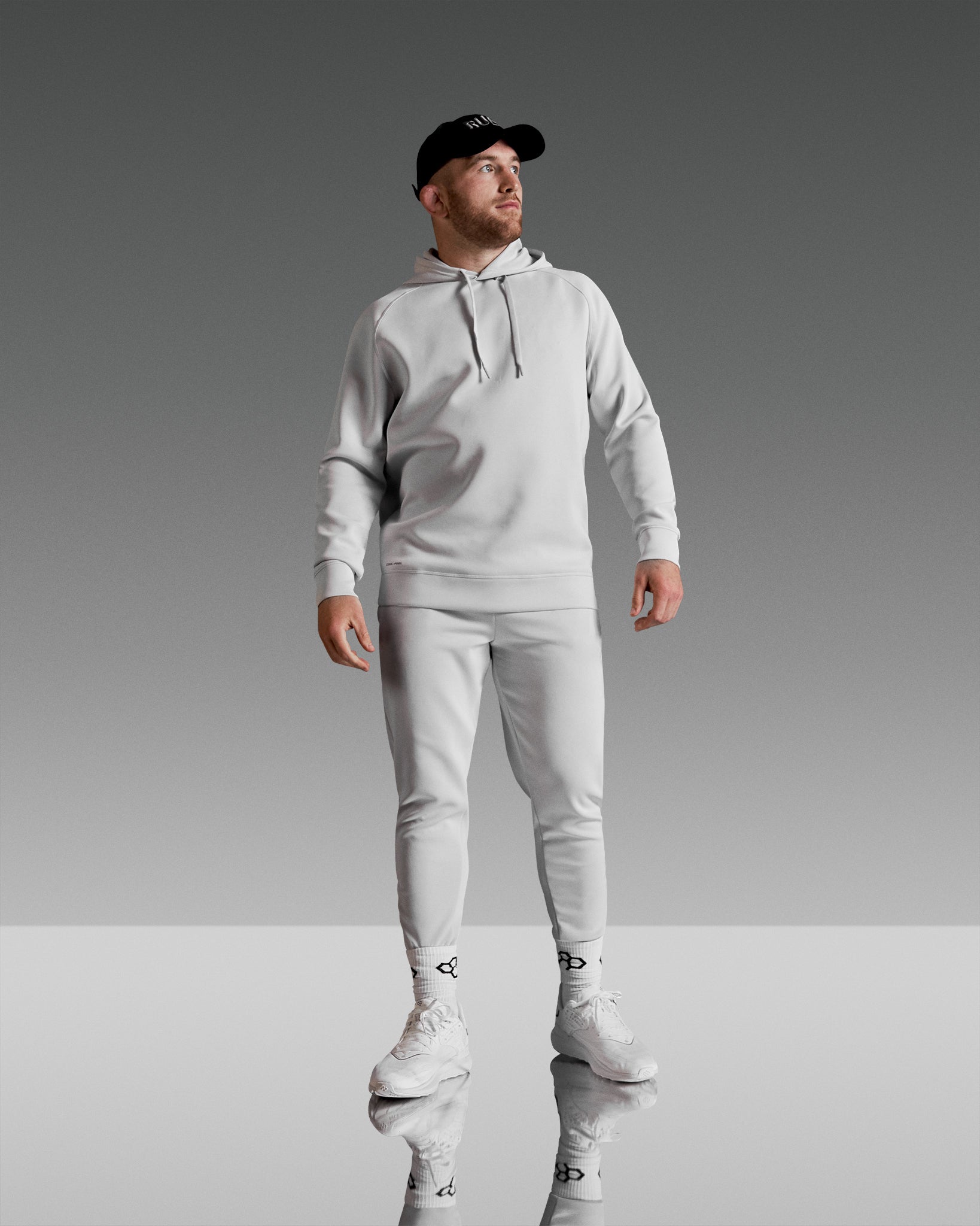 A man stands confidently in a stylish all-gray athletic outfit including a hoodie joggers and sneakers set against a sleek gradient background