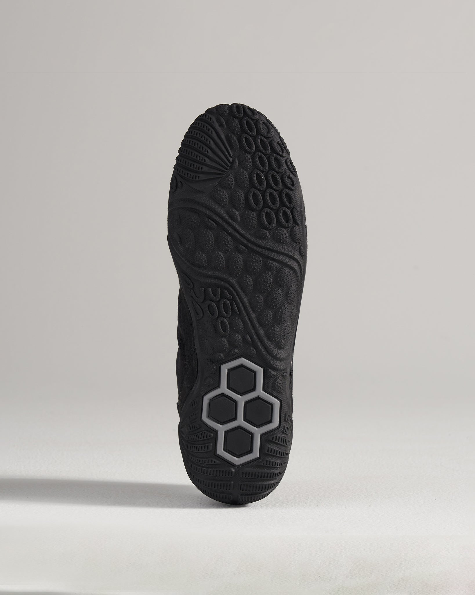 A close-up view of the textured sole of a black athletic shoe featuring distinctive grip patterns and a unique hexagonal design element in gray