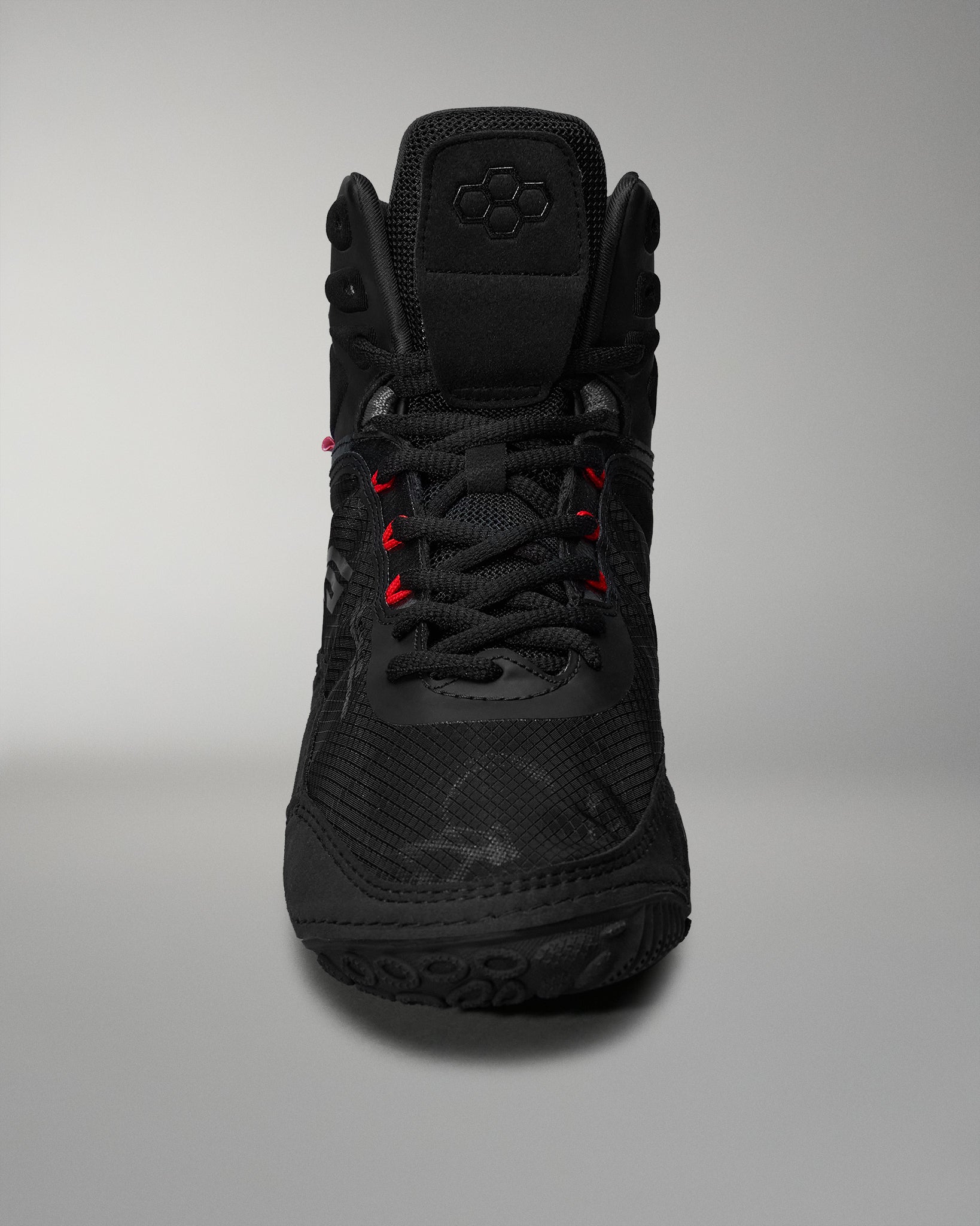 Front view of a high-top black athletic shoe with textured materials and contrasting red laces on a soft gray background.