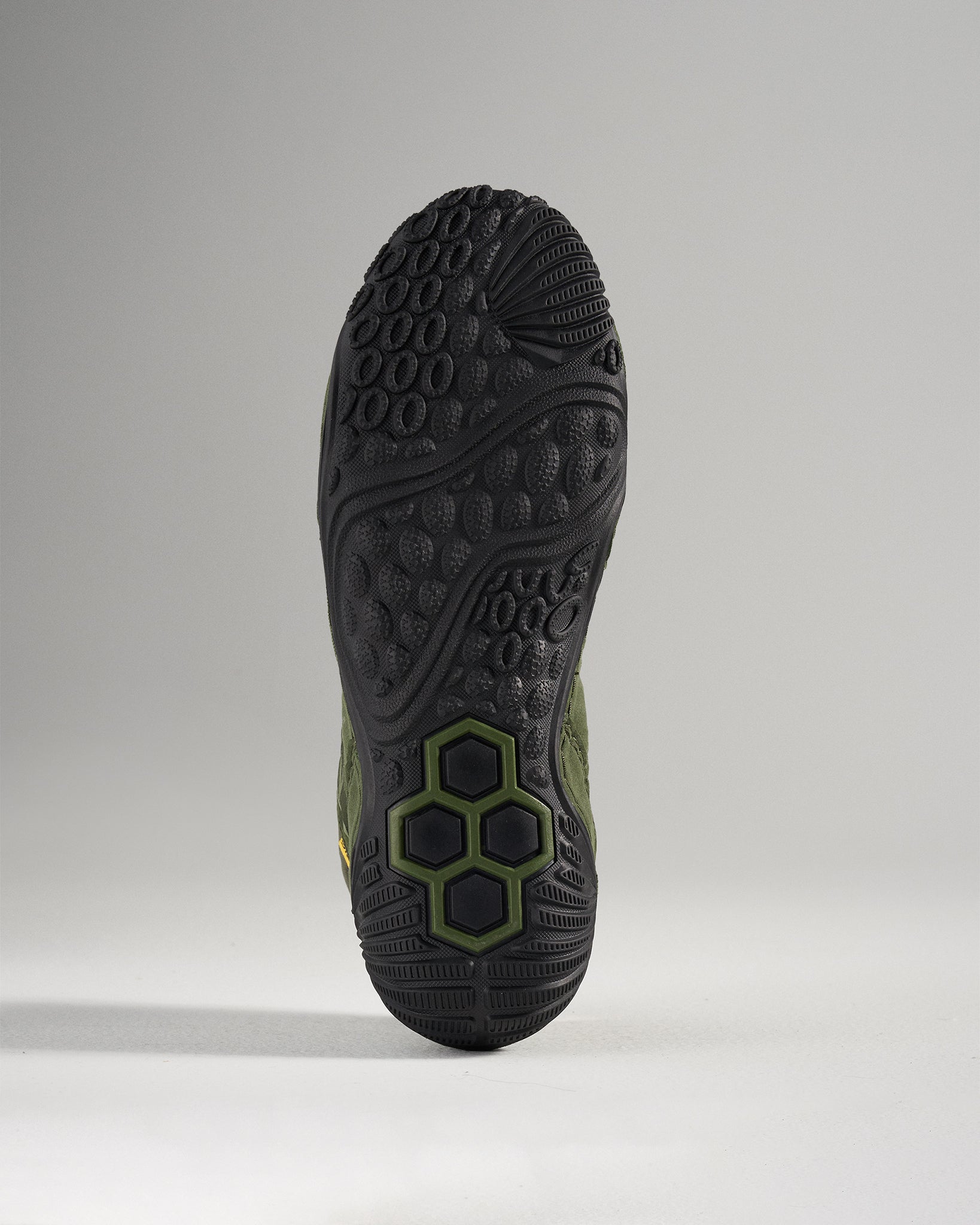 This image displays the underside of a rugged athletic shoe featuring a textured black sole with distinct traction patterns and greenish accents