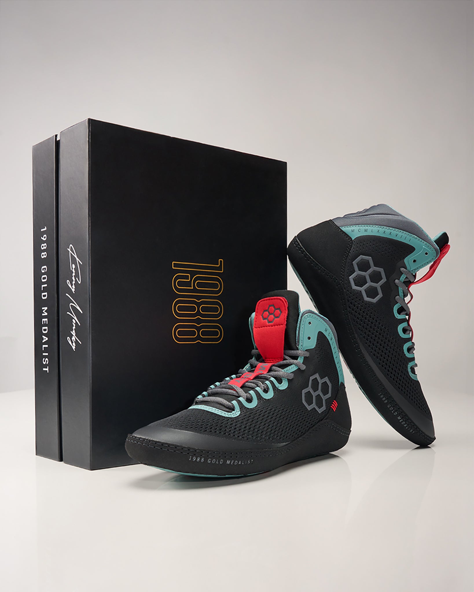 A pair of unique black and teal basketball shoes with red accents displayed next to a commemorative box labeled 1988 GOLD MEDALIST