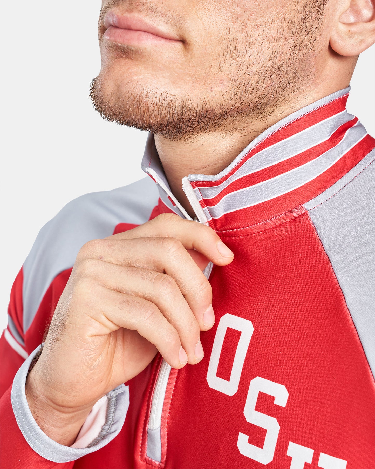 A close-up of a man adjusting the zipper of a red and gray athletic jacket showcasing the collar and logo