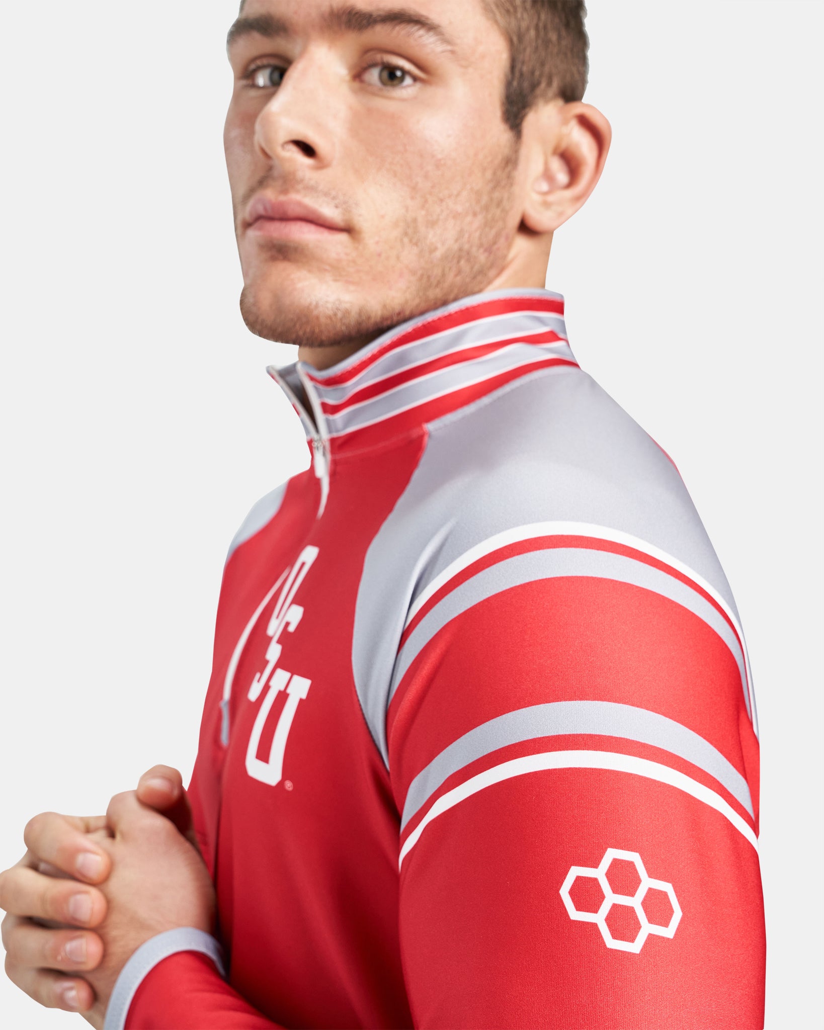 A young man poses in a red athletic top with gray accents and team logos showcasing a confident demeanor against a neutral background