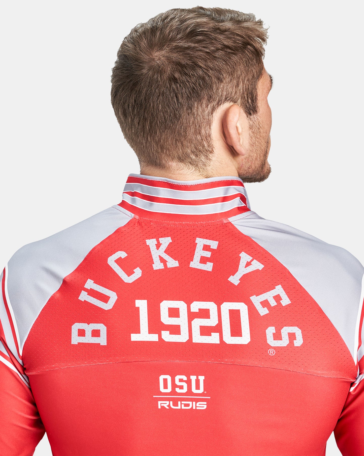 Rear view of a man wearing a red athletic wrestling jacket featuring BUCKEYES 1920 in bold lettering and OSU RUDIS branding at the bottom